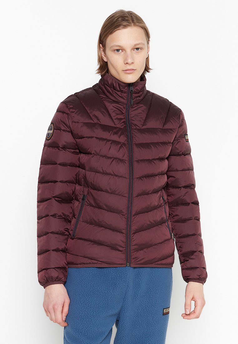 Giacca puffer bordeaux, materiale in nylon, colletto alto, sezioni cucite verticalmente, chiusura frontale con zip, tasche laterali, patch logo sulla spalla.
