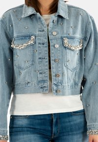 Chaqueta de mezclilla en azul claro con bolsillos adornados y strass dispersos. Diseño corto con cierres de botones y detalles en los puños.