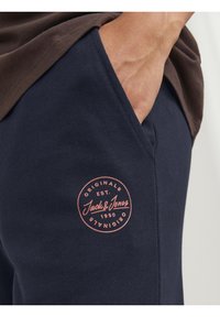 Mörkblå bomullssweatpants med en rund ficka och en rosa cirkulär logotypmärke med "Jack & Jones" och "EST. 1990." Mjuk textur.