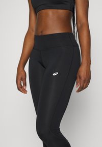 Leggings negros hechos de un material elástico y ligero con una textura suave, presentan un pequeño logo blanco y un diseño minimalista.