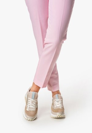 Beige sneakers with mesh and synthetic upper, white laces, blue accent, and textured sole, paired with pink fitted pants.