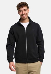 Svart zip-up sweatshirt i mjukt tyg med hög krage, utrustad med en subtil logotyp på bröstet samt elastiska muddar och nederkant.