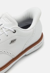 White sneaker with smooth synthetic upper, perforated detailing, brown rubber sole, and gray accents on the eyelets and logo.