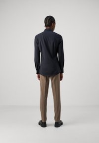 Schwarzes Langarmhemd mit klassischem Kragen und geknöpften Manschetten, kombiniert mit beigen maßgeschneiderten Hosen und schwarzen Schuhen. Glattes, figurschmeichelndes Design.
