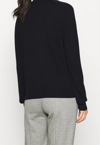 Suéter negro de punto con cuello redondo y mangas largas. Combinado con pantalones gris con patrón de espiga.