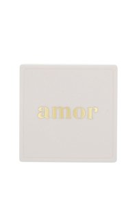 Kvadratisk keramisk underlägg i mjuk rosa, med ordet "amor" i prägling med guldfärgade bokstäver, inramat av en subtil kant. Slät yta.