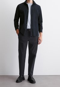 Czarna koszula zapinana na guziki noszona na jasnoniebieskim t-shircie, zestawiona z ciemnymi spodniami i czarnymi loafersami, charakteryzująca się gładkimi teksturami i dopasowanym krojem.