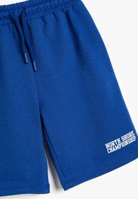 Blå bomulds shorts med elastisk talje og snor. Har hvid tekst "NORTH SHORE CHAMPIONSHIP" på nederste højre side.