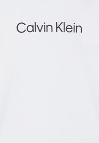 White cotton t-shirt featuring "Calvin Klein" printed in bold black letters. The fabric appears smooth with a classic round neckline.