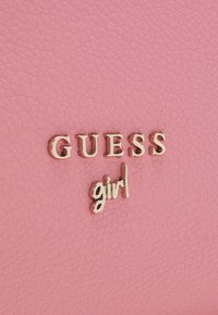 Similicuir texturé rose avec des lettres dorées « GUESS » et « girl ». Finition lisse, forme rectangulaire, sans motifs ou accents supplémentaires.
