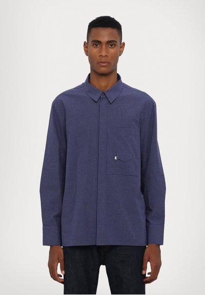 Camicia a scacchi blu navy con colletto, maniche lunghe e taschino sul petto. Presenta un piccolo dettaglio logo sulla tasca. Realizzata in tessuto leggero.