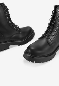 Black leather ankle boots with a rounded toe, featuring metal eyelets, laces, and a thick, textured rubber sole.