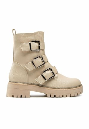 Beiger Leder-Stiefelette mit drei silbernen Schnallenriemen, dicker profillaufsohle und Zuggurt am Rücken.