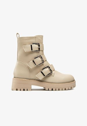 Beiger Leder-Stiefelette mit drei silbernen Schnallenriemen, dicker profillaufsohle und Zuggurt am Rücken.