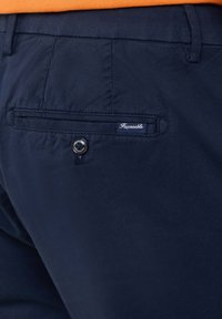 Pantaloni blu navy realizzati in tessuto liscio, con una tasca posteriore con chiusura a bottone e un'etichetta con logo in cucitura bianca.