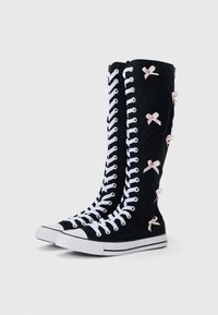 Mustad mustad tennised valgete paelte ja kummitaldadega, kaunistatud väikeste roosade paeltega külgedel ja voolujoonelise disainiga.