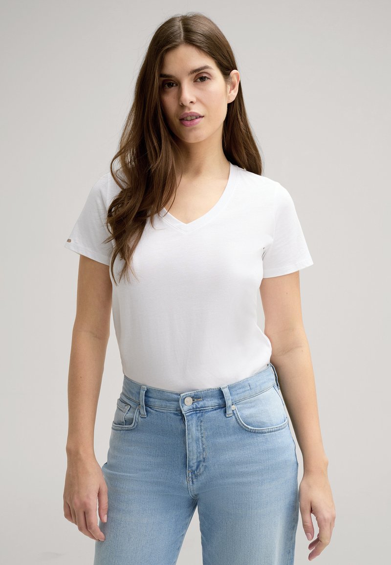 Witte V-hals t-shirt van zacht katoen, met korte mouwen en een ontspannen pasvorm, gecombineerd met lichtblauwe high-waisted jeans.