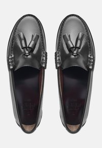Mocassins en cuir noir avec des détails à franges, présentant une finition lisse et un design cousu le long des bords. L'intérieur est doublé de marron.