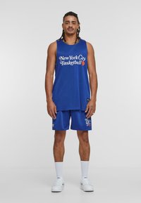 Blå basketballtrøye med mesh-struktur og hvit "New York City Basketball" trykk, parret med matchende shorts og hvite sokker og sko.