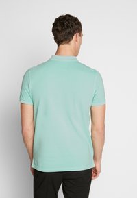 Miętowo-zielona koszulka polo z krótkimi rękawami, kołnierzykiem i subtelnymi detalami przeszyć. Gładka tekstura, prosty design, pokazany widok z tyłu.