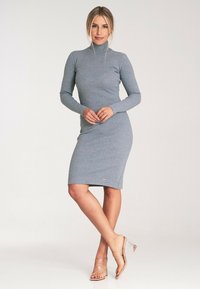 Szary, dopasowany golf z długimi rękawami, o długości do kolan, o miękkiej teksturze i małym logo na dole. Przezroczyste buty.