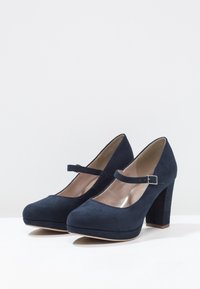 Escarpins Mary Jane en daim bleu marine avec un embout rond, une sangle à boucle et un talon épais. Texture lisse et détails minimaux.