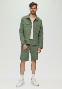 Groene katoenen shirt met korte mouwen en twee borstzakken, gecombineerd met bijpassende cargoshorts, gedragen met witte sneakers en enkelsokken.
