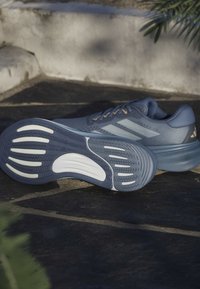 Blue athletic shoe with textured upper, contrasting laces, and a patterned rubber sole featuring white accents and grooves for traction.