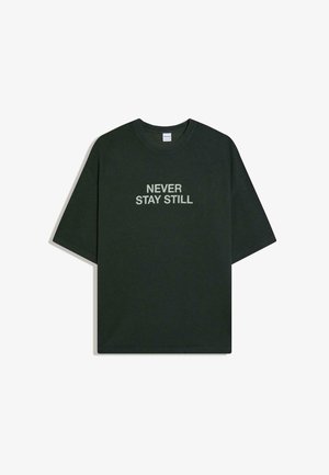 Tricou verde închis cu mâneci scurte, guler rotund și text alb "NEVER STAY STILL" centrat pe partea din față.