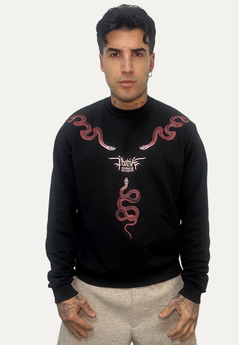 Felpa nera con grafiche rosa a forma di serpente sulle spalle e al centro, con logo brandizzato. Il materiale appare morbido e la vestibilità è comoda.