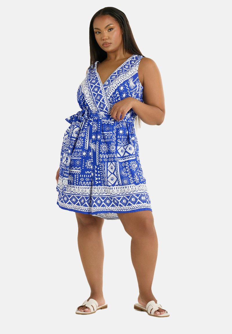 Abito estivo blu con motivo, scollatura a V profonda, accenti bianchi, cintura in vita e orlo svasato. Indossato con sandali piatti.