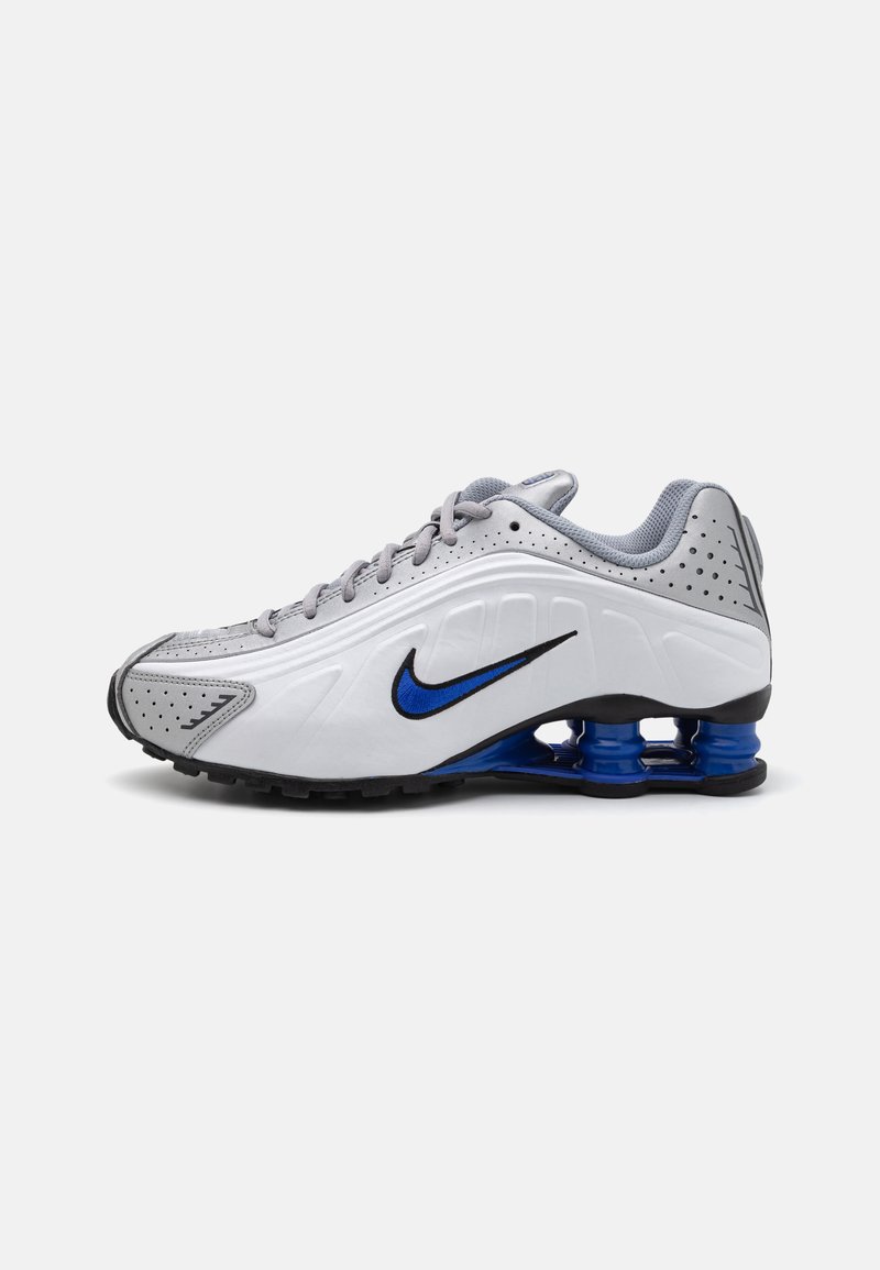 Nike Sportschuh mit grauem Synthetik-Obermaterial, schwarzer Laufsohle, blauen Kunststoff-Fersenschutz und perforierten Details zur Belüftung.