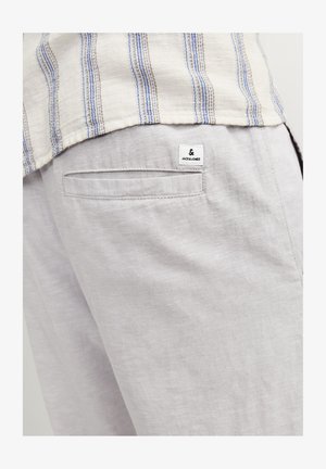 Pantaloni di lino grigio chiaro con una tasca posteriore e un piccolo etichetta di marca. Il tessuto ha un aspetto morbido e texture.