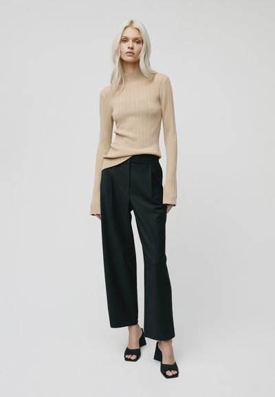 Top lungo a maniche lunghe beige a coste con scollatura alta, abbinato a pantaloni neri a gamba larga e scarpe con tacco a blocco aperte nere.