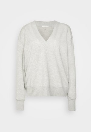 Harmahtava, ylipitkä collegepaita V-kauluksella, yhdistetty tummansinisiin slim fit -farkkuihin ja mustiin hihnakenkiin. Sujuvat tekstuurit ja rento istuvuus.