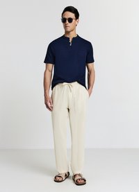 Maglietta henley maniche corte blu navy, pantaloni crema con coulisse e sandali marroni. Vestibilità slim, tessuto strutturato, bottoni a vista e tasche laterali.