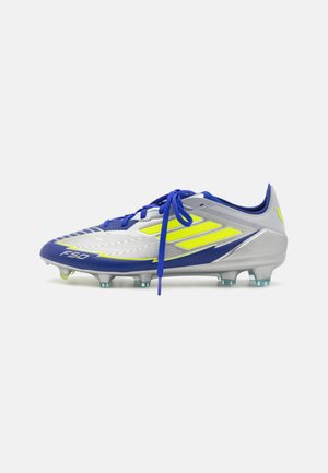 Scarpini da calcio blu e argento con tomaia testurizzata, tre strisce gialle e suola moldata con tacchetti trasparenti. Presentano lacci blu e marchio.