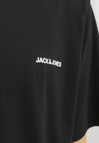 Czarna bawełniana koszulka z krótkim rękawem z białym logo "JACK & JONES" na lewej stronie klatki piersiowej. Miękka tekstura i standardowy fason.