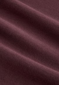 Bordó színű szövet sima, puha textúrával, finom redőkkel és kontúrokkal, amelyek mélységet és gazdagságot sugároznak a színben.
