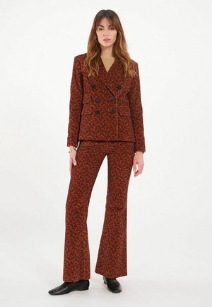 Blazer double-breasted à motifs floraux rouges et pantalon évasé assorti, avec des boutons noirs et une texture lisse. Chaussures noires.