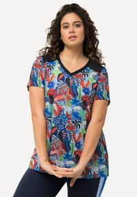 Camiseta de manga corta colorida con un estampado floral y botánico en rojo, azul, verde y negro, con un cuello en V azul marino y mangas en contraste.