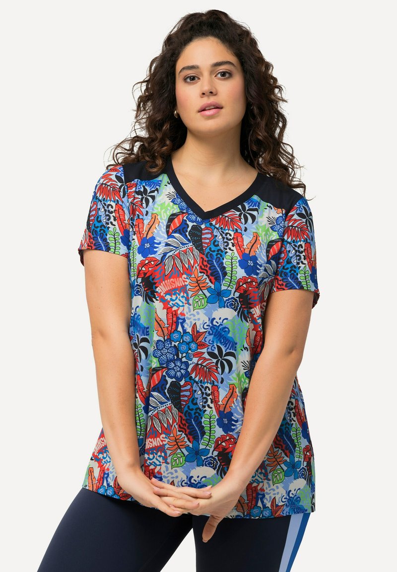 Camiseta de manga corta colorida con un estampado floral y botánico en rojo, azul, verde y negro, con un cuello en V azul marino y mangas en contraste.