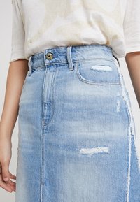 Ljusblå denimkjol med slitna detaljer, hög midja, fem fickor och hyskslås i mässing. Slät textur och A-linjeform.