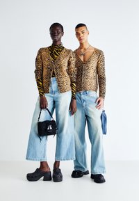 Luipaardprint vestjes, gele en zwarte gestreepte coltrui, lichtblauwe wijde jeans, zwarte tassen en schoenen. Soepele en gestructureerde stoffen.