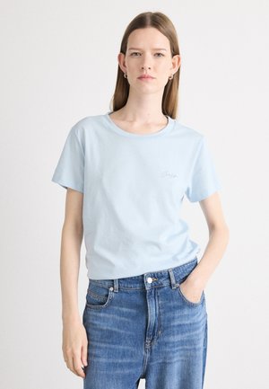 Svetlo modra bombažna majica s krojem, kratkimi rokavi in subtilnim vezenim detajlom na levem prsnem delu, v kombinaciji z visokim pasom denim hlačami.