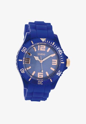 Blue silicone watch with a circular face, rose gold markers and hands, featuring a date window at 3 o’clock and a textured bezel.