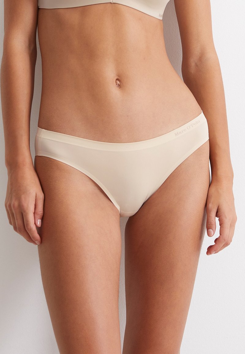 Slip beige senza cuciture realizzati in tessuto liscio, con taglio a vita bassa e una cintura minimalista con logo del brand.