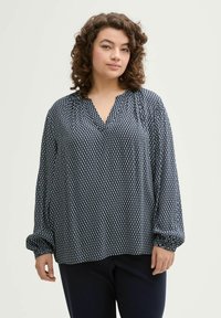 Blusa de color azul marino con un patrón geométrico blanco, escote en V y mangas largas con gather. Tejido suave y ligero con un corte holgado.