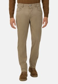 Beżowe bawełniane spodnie o prostym kroju, z frontowymi kieszeniami i zapięciem na guzik. Noszone z brązowymi butami i swetrem.