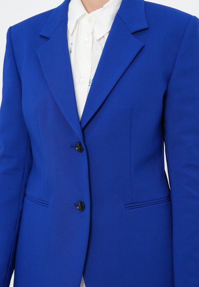 Royal blue tailored blazer with a structured design, sharp lapels, and two black buttons. Features side pockets and smooth fabric texture.